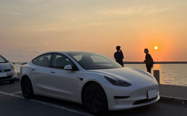 沖縄で夕日を楽しむテスラ車と旅行者