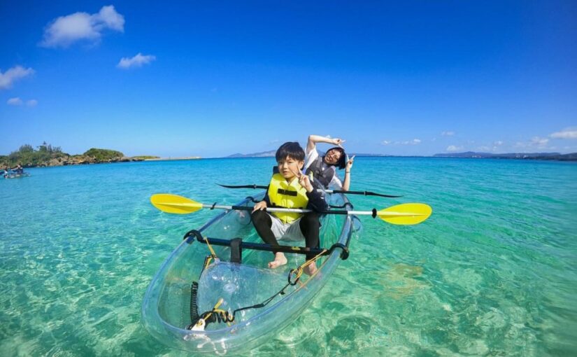 沖縄の青い海を背景に、スケルトンのカヤックでピースサインをする親子