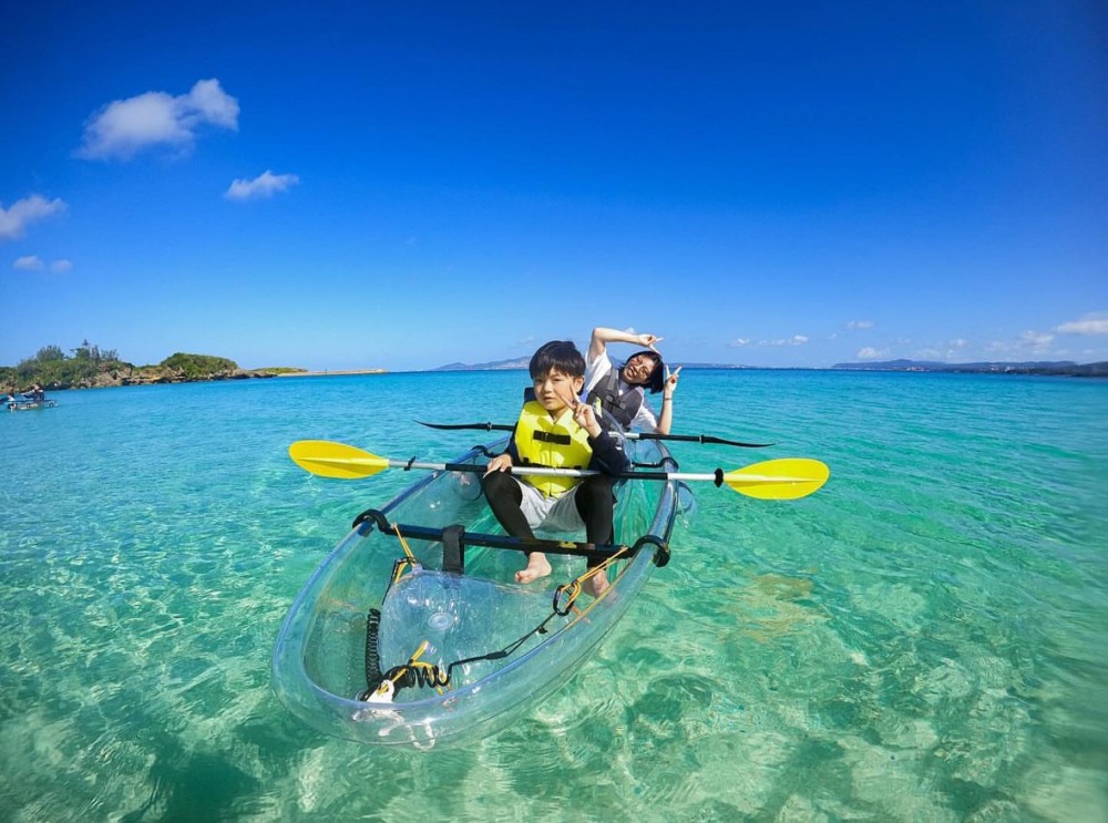 沖縄の青い海を背景に、スケルトンのカヤックでピースサインをする親子