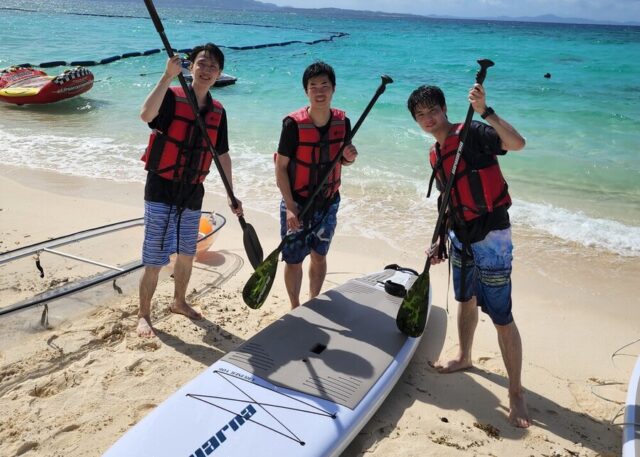 伊江島ツアーの美しいビーチでサップ(SUP)の準備をする3人の男性