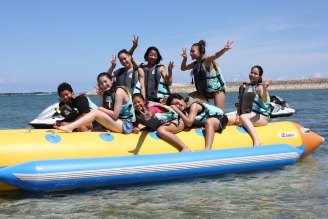 伊江島　黄色いバナナボートの上でポーズをとるライフジャケット姿の男女グループ