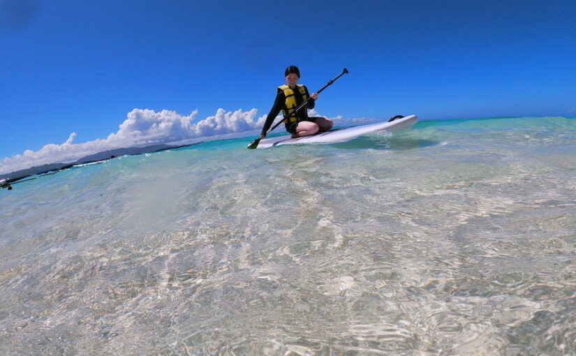 伊江島の透き通った浅瀬で、SUPを漕ぎながら海を楽しむアクティビティシーン