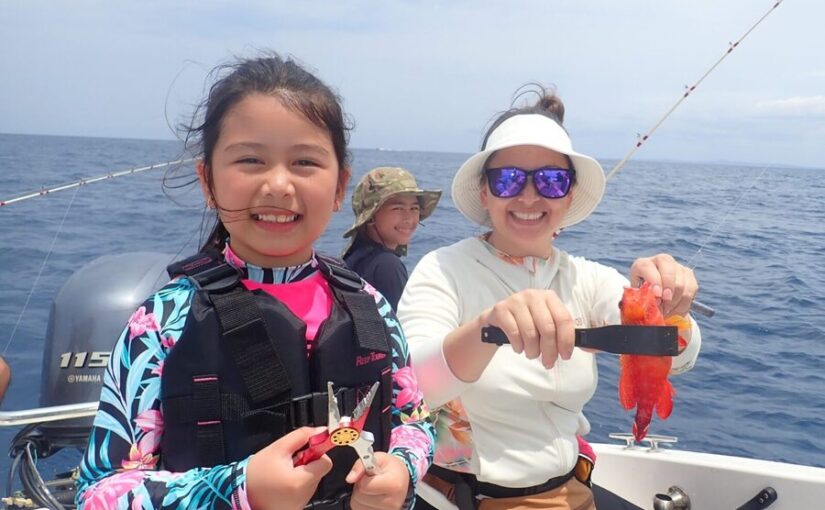 船釣りで真っ赤なミーバイ（ハタ）を釣り上げ、笑顔を見せる親子
