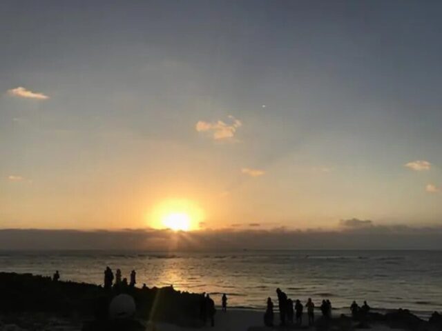 沖縄の海岸で水平線から昇る朝日と、日の出を待つ人々のシルエット