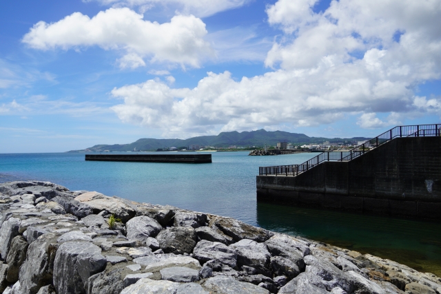 青い海に囲まれた沖縄の石積み堤防と階段状の護岸。遠くに島影が見える絶好の釣りポイント。