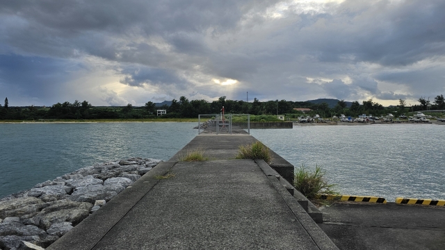 夕暮れ時の静かな漁港の突堤。雲の間から光が差し込む幻想的な釣り場の雰囲気。
