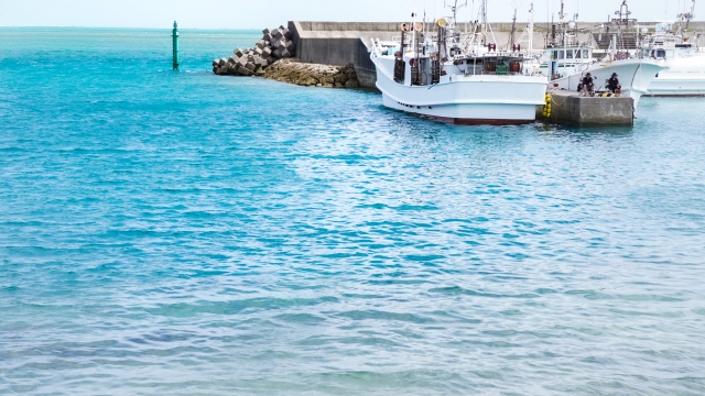 ターコイズブルーの海に面した漁港の防波堤と、停泊している白い漁船
