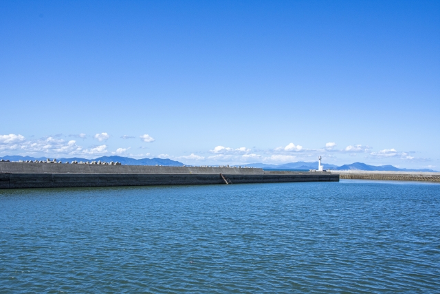 真っ青な空と水平線が広がる沖縄の防波堤。白い灯台が目印の広々とした潮通しの良い釣り場。