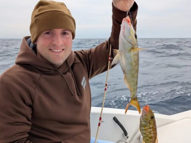 沖縄の海上で釣り上げた2匹の魚を掲げて笑顔を見せる男性アングラー